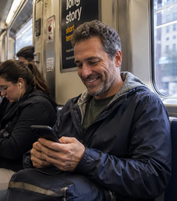 Man smiling at his phone on the train